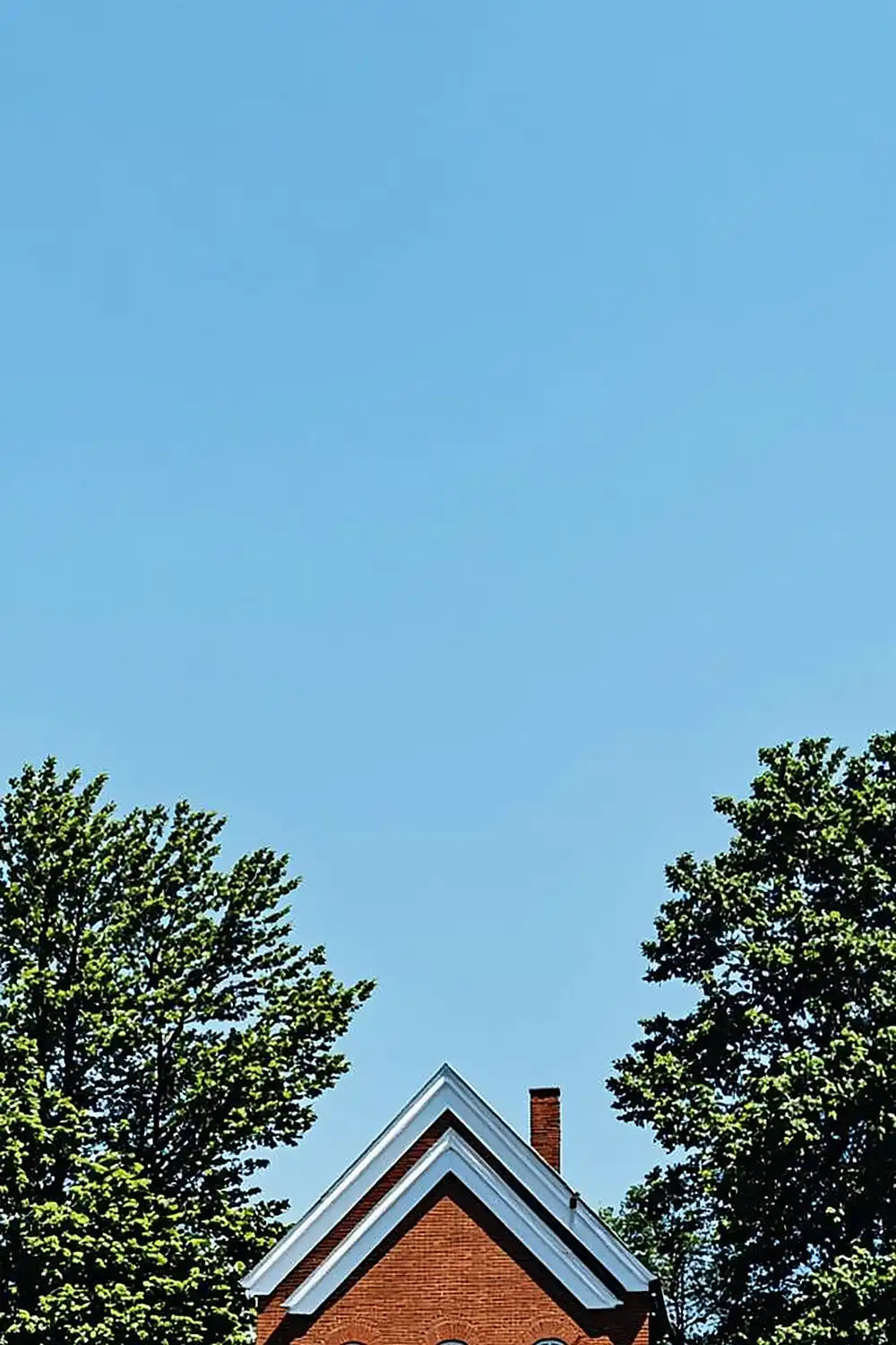 Brick schoolhouse with trees under a clear blue sky