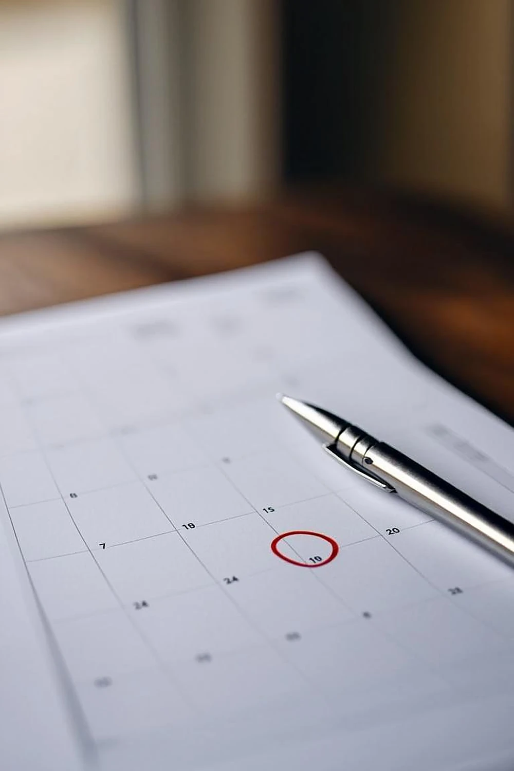 Wall calendar with circled dates beside a fountain pen on a wooden desk