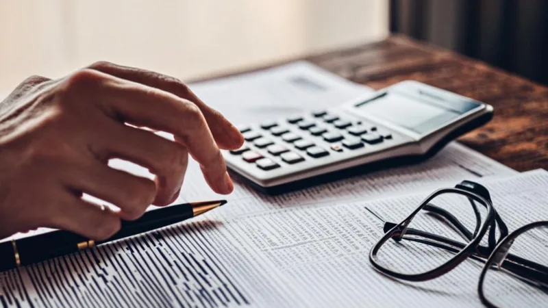 Close-up of hands using a calculator over a financial worksheet on a wooden desk